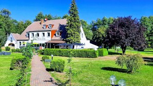 A large, white building with a sign reading "RURALANK" and a paved pathway leading to it. - Landhotel Prälank (Neustrelitz)
