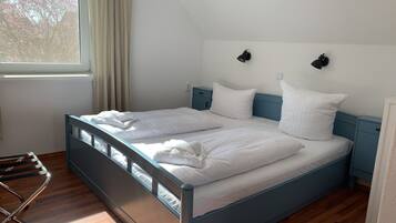 A double bed with white linens, a wooden floor, a blue headboard, and a nightstand with a lamp.