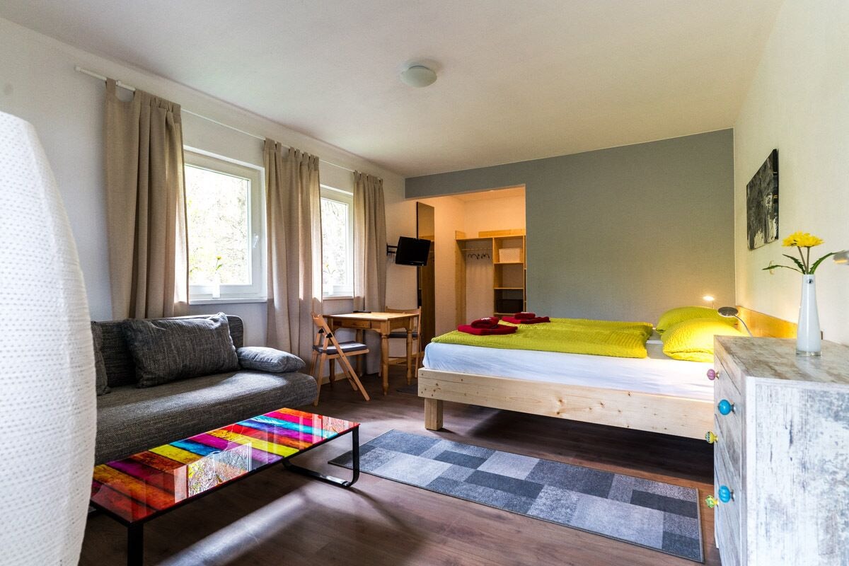 Une chambre à coucher de taille réduite, comprenant un lit, un canapé, une petite table et un téléviseur.