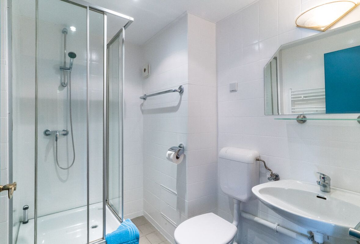 Une salle de bain moderne avec une douche à parois de verre, des toilettes blanches et un lavabo surmonté d’un miroir.