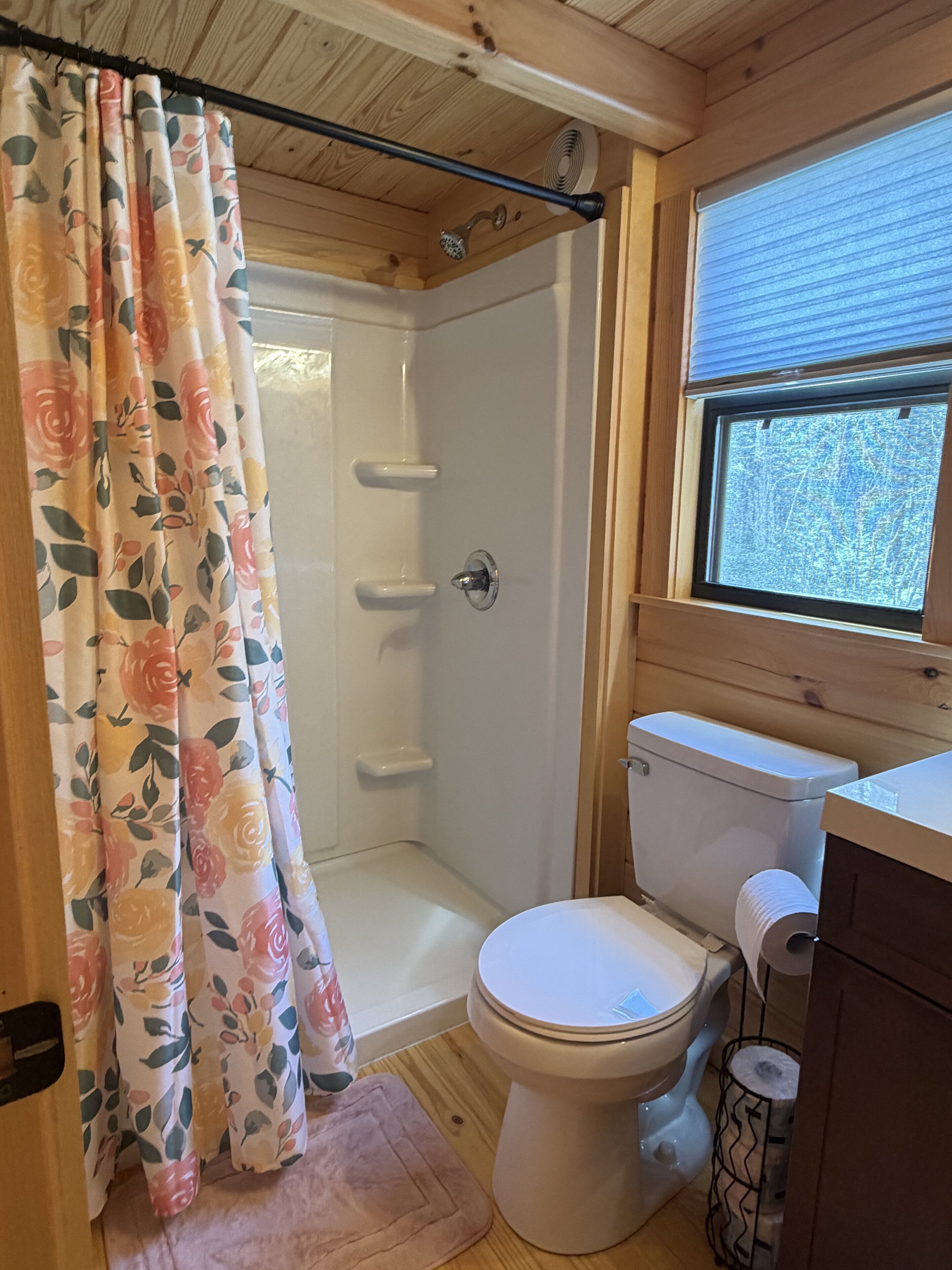 A wooden cabin bathroom with a shower, toilet, and window.