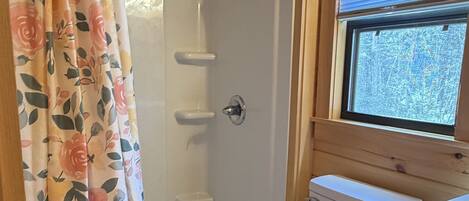 A wooden cabin bathroom with a shower, toilet, and window.