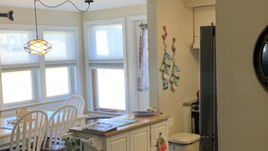 A kitchen with a dining table, chairs, a white cabinet, a refrigerator, and a hanging light fixture.