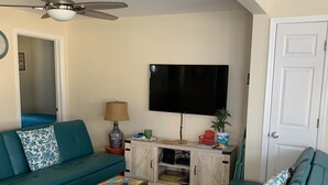 A living room with teal sofas, a flat-screen TV, a ceiling fan, and a cabinet with various items.