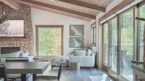 A spacious living area with a large dining table, comfortable seating, a stone fireplace, and large windows offering views of the outdoors. - Dreamy home on river, mountain views, steps from town. (Frisco)