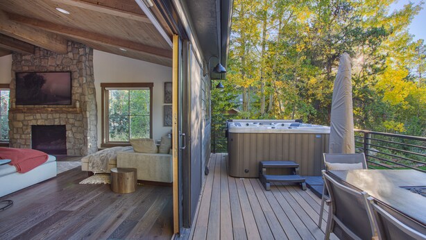 A deck with a hot tub, outdoor seating, and a stone fireplace. - Dreamy home on river, mountain views, steps from town. (Frisco)