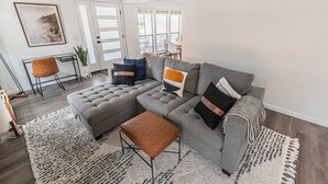 Een moderne woonkamer met een hoekbank, een voetenbankje en een groot vloerkleed.