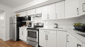A modern kitchen with stainless steel appliances, white cabinetry, and a wooden floor.