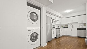 A modern kitchen with white cabinetry, a stainless steel refrigerator, an oven, and a dishwasher.