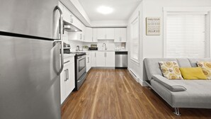A modern kitchen with stainless steel appliances, white cabinetry, and a grey sofa with yellow cushions.