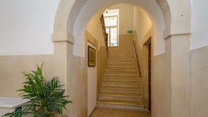 En smal hall med en trappa som leder upp till en våning ovanför. En krukväxt står till vänster, och en inramad tavla hänger på väggen.