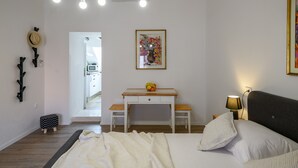 Ett sovrum med en säng, ett nattduksbord, en lampa och ett skrivbord med en stol. Det finns en tavla på väggen och en hatt som hänger på väggen.