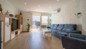 A modern living room with a grey sofa, wooden cabinets, a flat-screen TV, and a potted plant. - HomeHolidaysRentals Benoit - Costa Barcelona (Pineda de Mar)