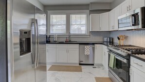 Una cocina moderna con gabinetes blancos, electrodomésticos de acero inoxidable, un microondas y una estufa a gas.