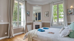 Een slaapkamer met een groot bed, een open haard en meerdere ramen.