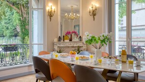 Een eetgedeelte met een marmeren tafel, oranje stoelen en uitzicht op groen.