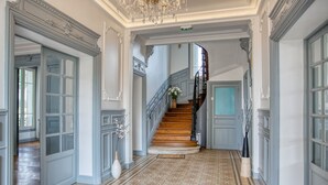 Een statige hal met een houten trap, gedetailleerd sierwerk en vloerbekleding met een patroon.