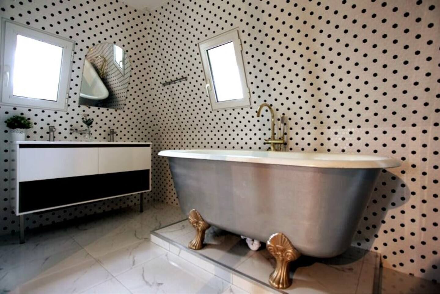A bathroom with a freestanding bathtub, a white vanity with a black base, and a polka dot wall.
