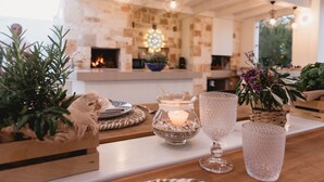 Eine gemütliche Küche mit Steinwand, Kamin und Hängeleuchten. Auf der Arbeitsplatte befinden sich Pflanzen und eine Kerze.