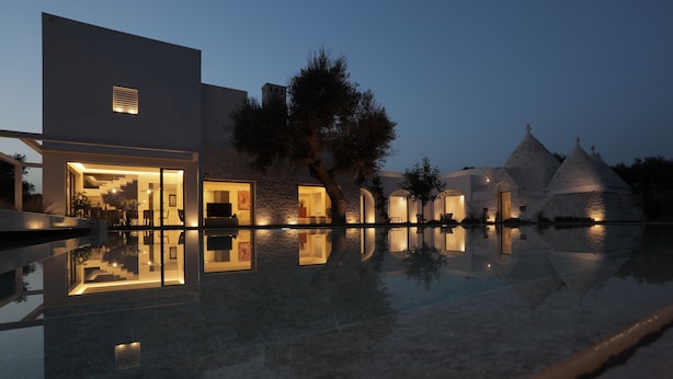 Ein modernes Hotel mit Glasfassade, einem Pool und einem dahinterliegenden Gebäude mit Kegeldächern.