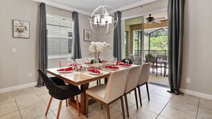 A dining room with a wooden table set for six, grey curtains, and a ceiling fan. - 6BR Villa|Saltwater Pool•Movie Theater|Disney (Kissimmee)