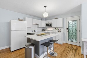 A modern kitchen with white cabinets, a central island with stools, a stainless steel refrigerator, and a microwave.