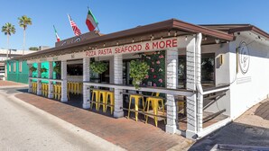 A restaurant with outdoor seating, a signboard for pizza pasta and seafood, and a flag display.