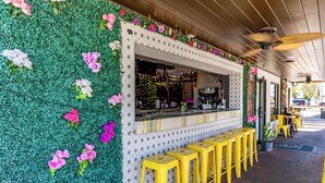 A restaurant with a green wall decorated with flowers, a bar counter, and yellow stools.