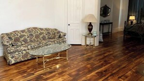 Ein Wohnzimmer mit einem blumengemusterten Sofa, einem Glastisch und einer Lampe auf einem Beistelltisch.