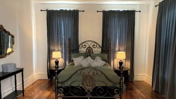 Ein Zimmer mit Himmelbett, zwei Nachttischlampen, einem kleinen Tisch mit Lampe und einem Spiegel an der Wand.