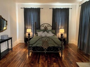 Classic four-poster bed with bedside tables and lamps, set against a backdrop of dark curtains and a mirror.
