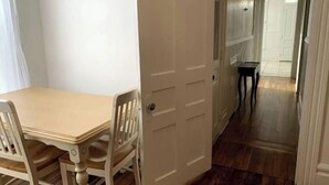 Ein Essbereich mit einem Holztisch und Stühlen, einer weißen Tür und einem Gang zu einem weiteren Raum.
