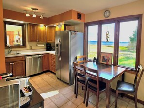 A kitchen with wooden cabinets, a stainless steel refrigerator, a dishwasher, and a dining table with chairs.