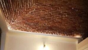 Una camera da letto con soffitto in mattoni, un letto con coperta grigia e due abat-jour.