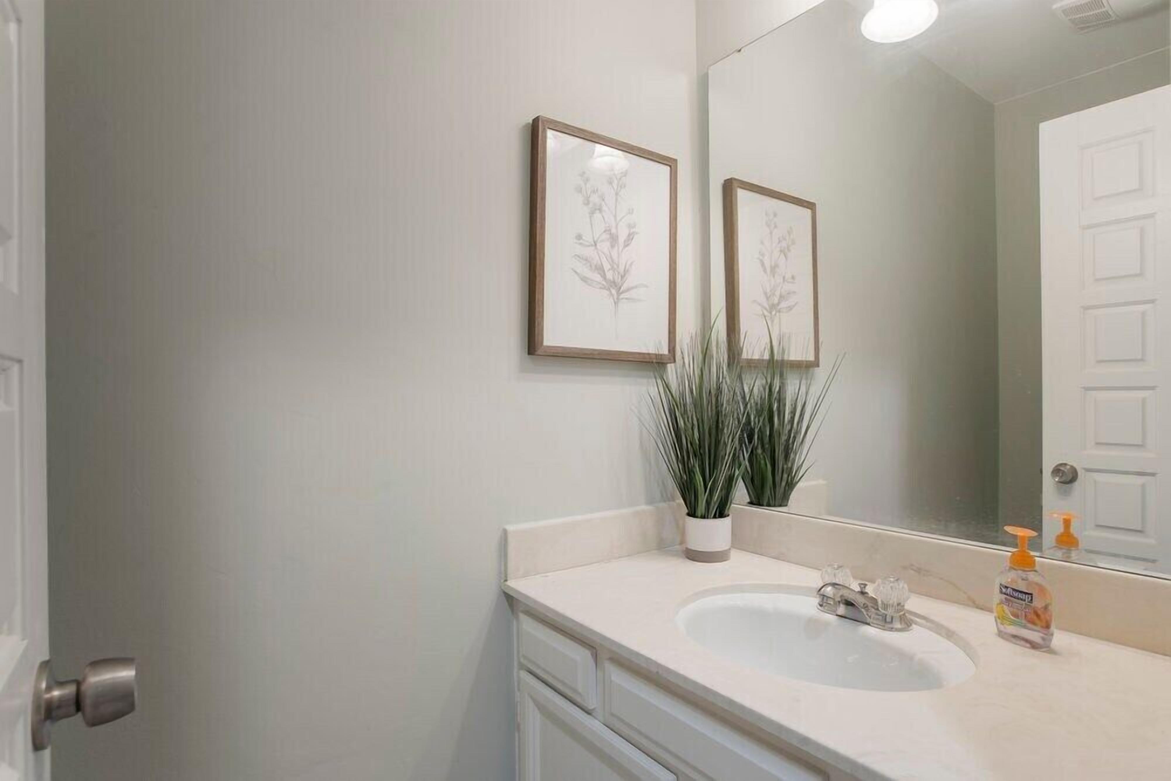 A bathroom with a white sink, a mirror, and two framed floral pictures on the wall.