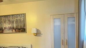 Et soveværelse med seng, natbord, lampe, garderobe og et billede på væggen.