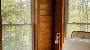A bedroom with a bed, a nightstand, and a window with a view of trees. - Charming Cottage with Jacuzzi, Fire Pit and Access to Nearby Lakes! (Monticello)