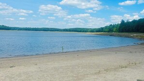 A wide, calm lake with a sandy shore and a forested area in the background. - Charming Cottage with Jacuzzi, Fire Pit and Access to Nearby Lakes! (Monticello)