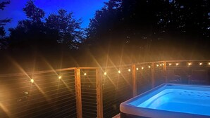 A hot tub on a wooden deck with string lights. - Charming Cottage with Jacuzzi, Fire Pit and Access to Nearby Lakes! (Monticello)