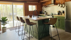 A modern kitchen with a central island, bar stools, a stainless steel refrigerator, and hanging pots. - Charming Cottage with Jacuzzi, Fire Pit and Access to Nearby Lakes! (Monticello)