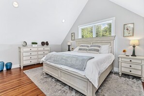 A bedroom with a large bed, white nightstands, a dresser, and a window with blinds. - Hilltop Haven w/ Hot Tub, Mountain Views & Game Room (Black Mountain)