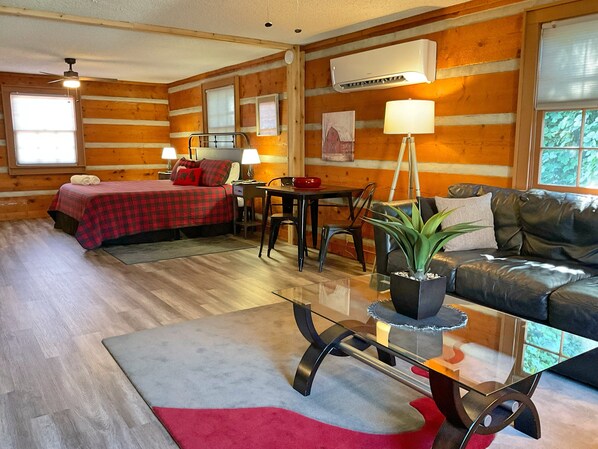 Ein Blockhaus-Interieur mit einem Bett, einer Couch, einem Esstisch und einer Topfpflanze.