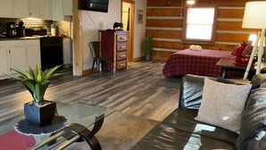 A compact living space with a kitchenette, a bed with a red checkered bedspread, a leather sofa, and a dining area with a glass table. - Studio B on Main St in Helen - Walkable to restaurants and attractions (Helen)