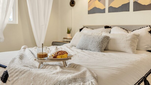 Ein ordentlich bezogenes Bett mit einem Tablett mit Speisen und Getränken, einer Lampe und Wandbildern mit Bergmotiv.
