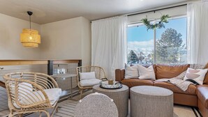 Ein modernes Wohnzimmer mit einem Korbstuhl, einem braunen Ledersofa und runden Hocker.