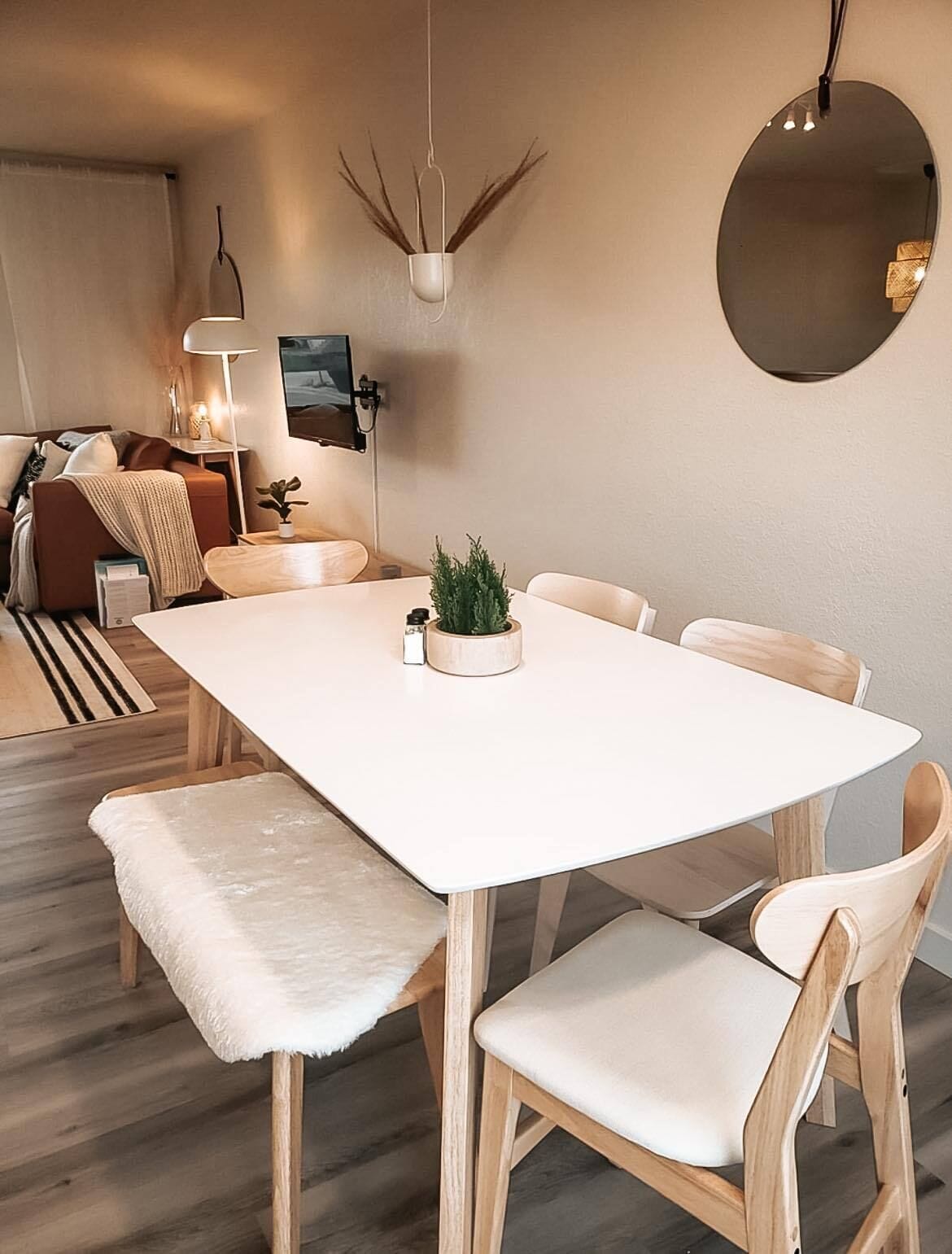 A modern dining area with a white table, wooden chairs, and a bench with a fur throw.