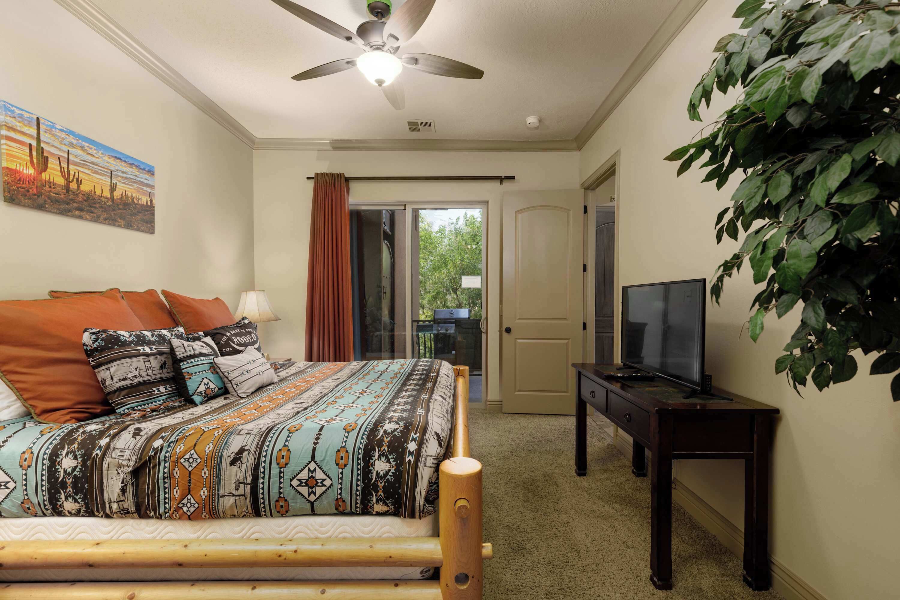 A bedroom with a bed, a television, a ceiling fan, a door, and a window.