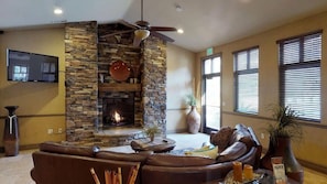 A living room with a stone fireplace, leather sofa, and a television mounted on the wall. - Top Floor Privacy | Outdoor Fireplace, Sleeps 8 (Hurricane)