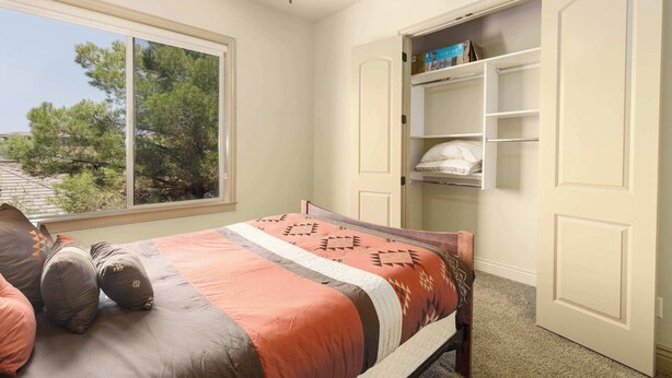 Een slaapkamer met een bed, een raam, een plafondventilator en een inbouwkast.