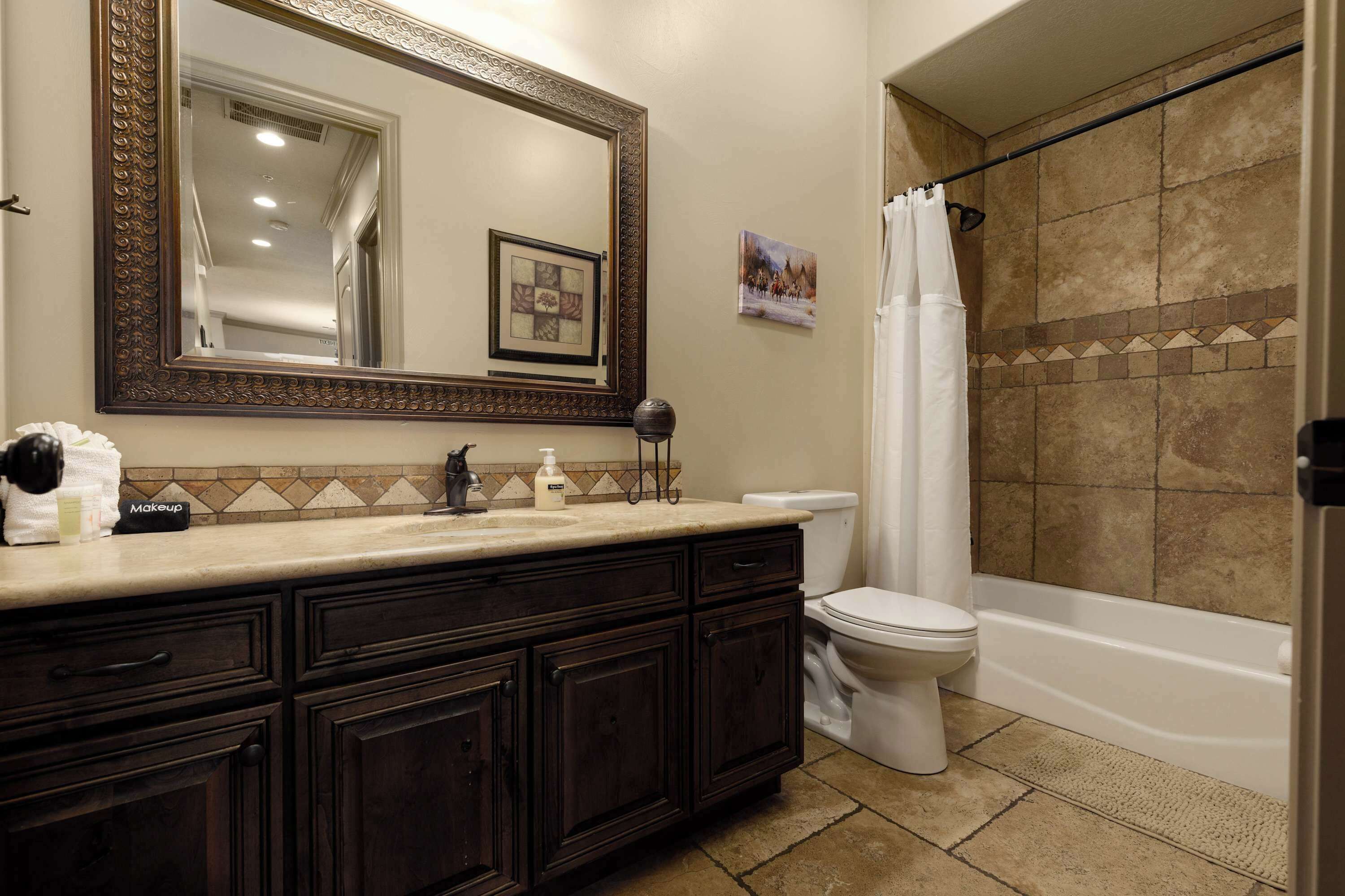 A bathroom with a dark wood vanity, a white toilet, and a shower with a beige tiled wall.